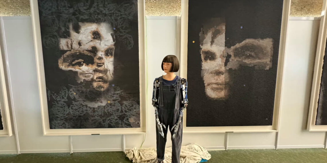 Робот Ai-Da на фоне портретов Тьюринга. Работа "AI God. Портрет Алана Тьюринга", которая была продана, висит справа. Фото: Sotheby's/EPA